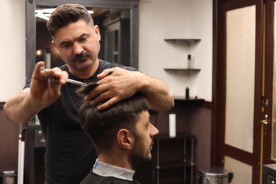 Photo of Professional hairdresser cutting man's hair in barbershop