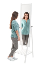 Young woman looking at her reflection in mirror on white background