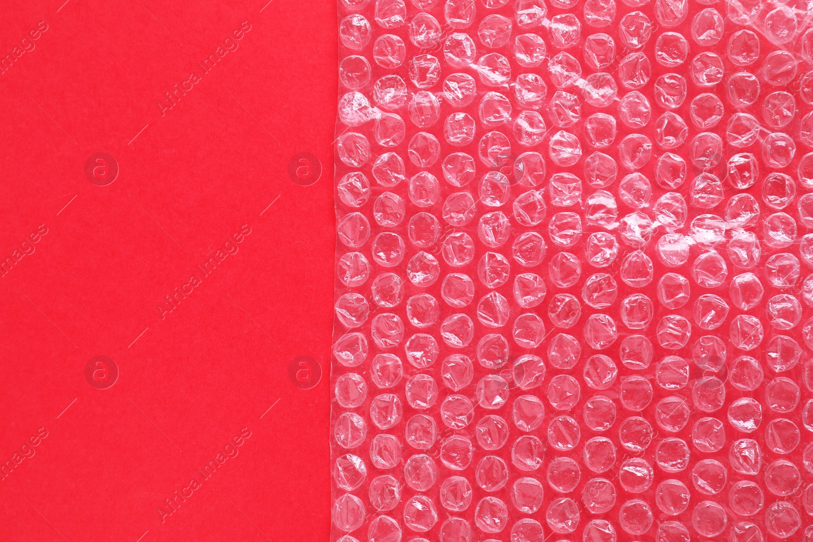 Photo of Transparent bubble wrap on red background, top view. Space for text