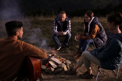 Photo of Group of friends gathering around bonfire at camping site in evening