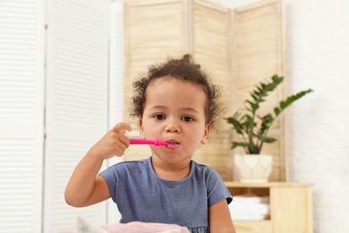 Photo of Cute African-American girl with toothbrush on blurred background