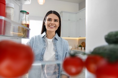 Photo of Young woman near refrigerator in kitchen, view from inside