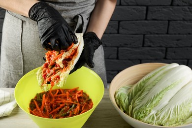 Photo of Woman preparing spicy cabbage kimchi at wooden table indoors, closeup