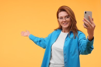 Photo of Beautiful woman in eyeglasses taking selfie on orange background. Space for text
