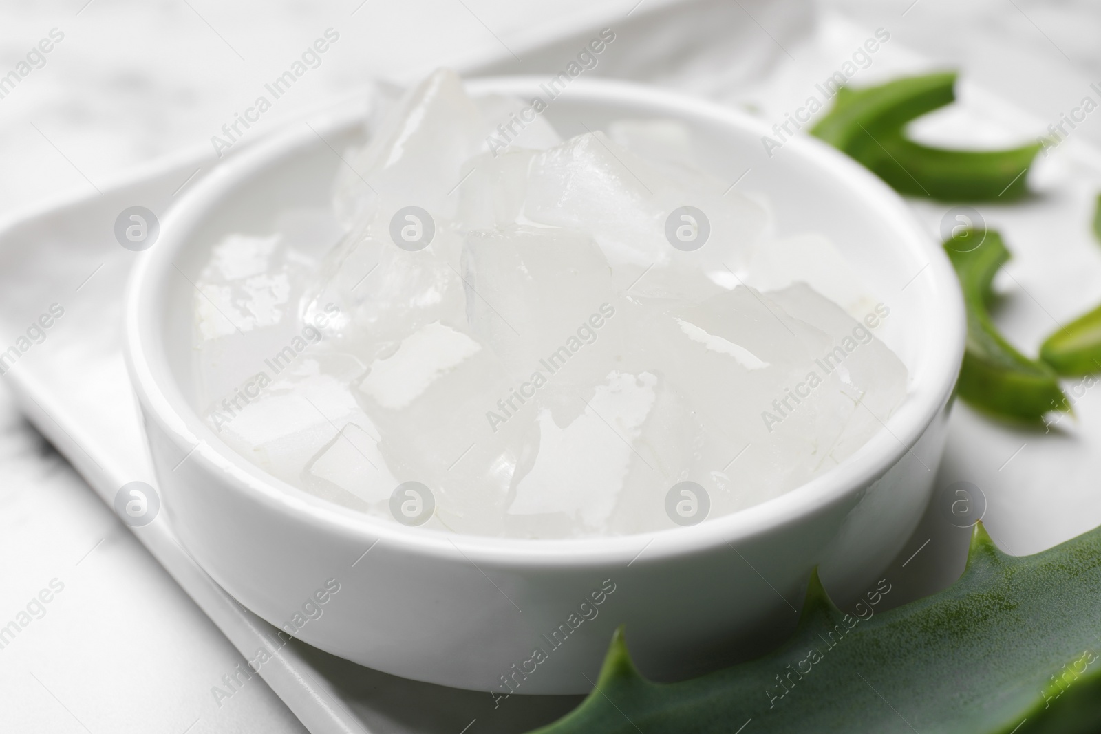 Photo of Aloe vera gel and slices of plant on white table, closeup