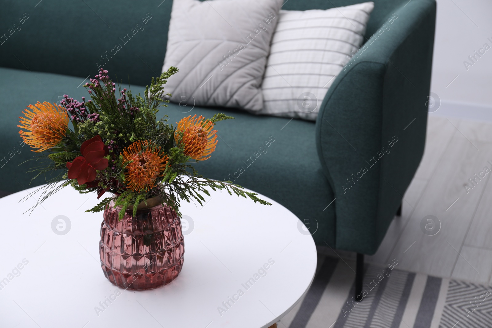 Photo of Vase with bouquet of beautiful leucospermum flowers on white coffee table in living room