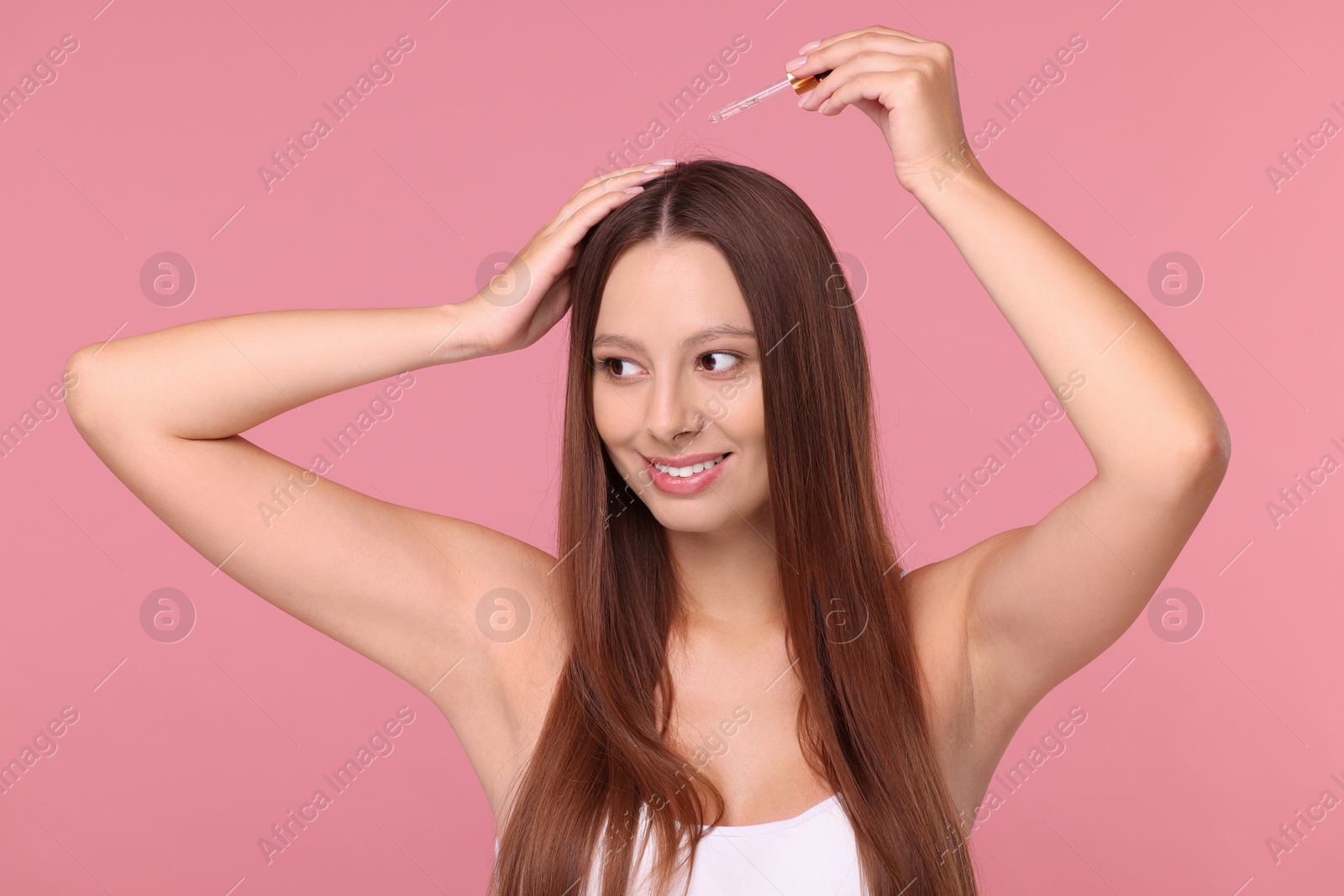 Photo of Beautiful woman applying serum onto hair on pink background