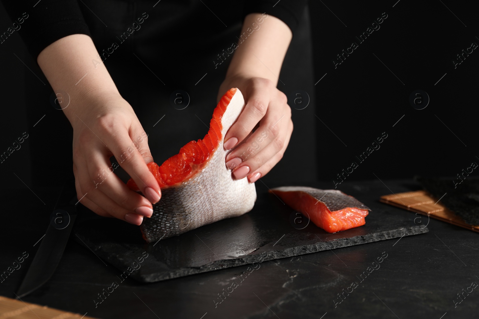 Photo of Chef taking salmon for sushi at dark textured table, closeup