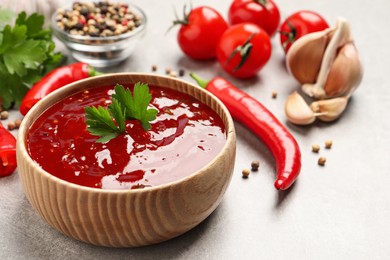 Photo of Spicy chili sauce with parsley in wooden bowl on light grey table, space for text