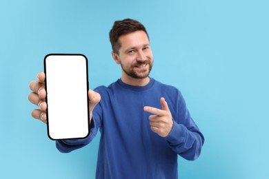 Handsome man showing smartphone in hand and pointing at it on light blue background, selective focus. Mockup for design