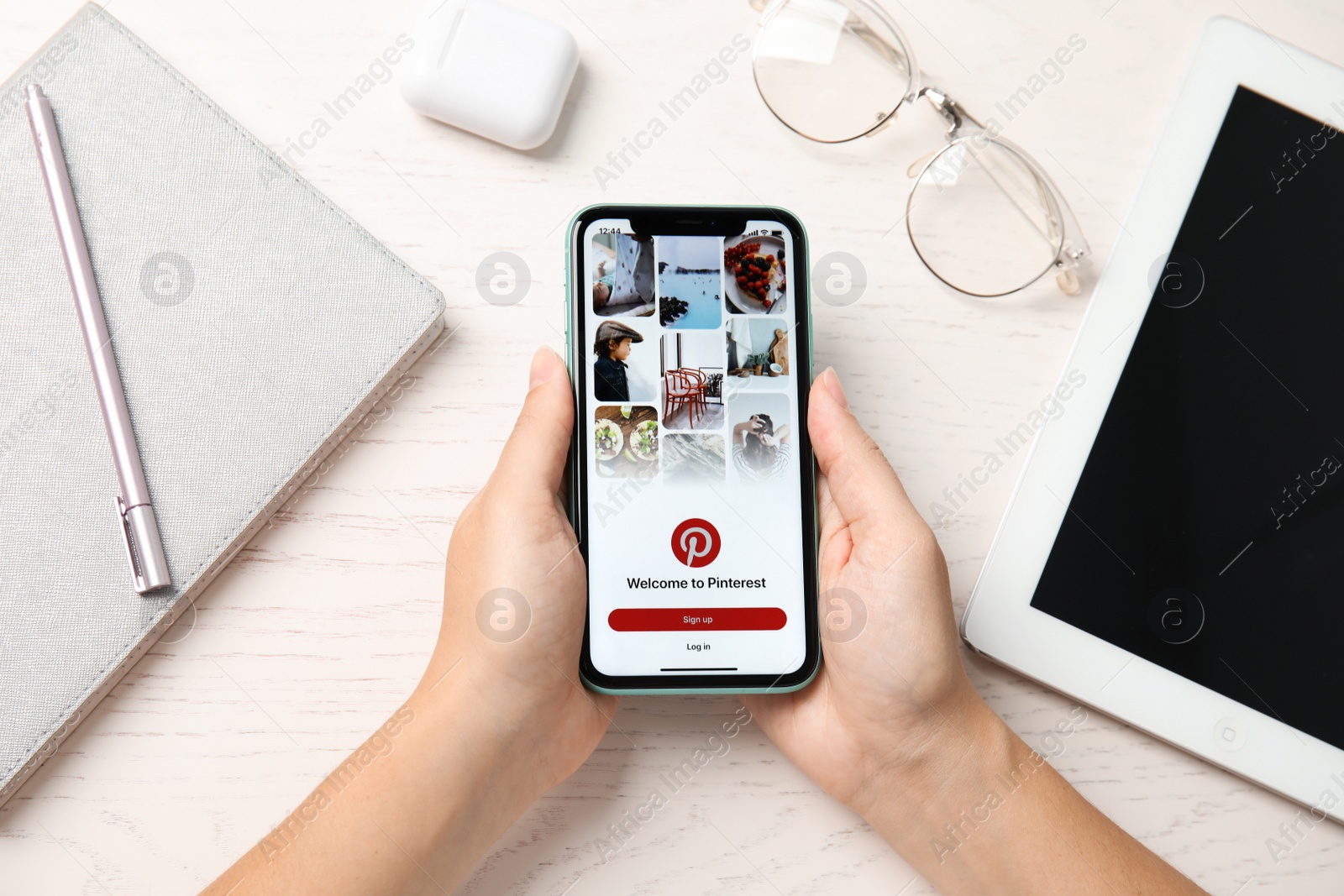 Photo of MYKOLAIV, UKRAINE - JULY 10, 2020: Woman holding Iphone 11 with Pinterest app on screen at table, top view