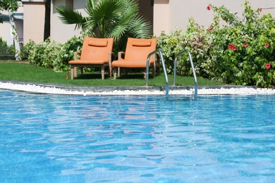 Photo of Sunbeds near modern swimming pool with stairs, outdoors