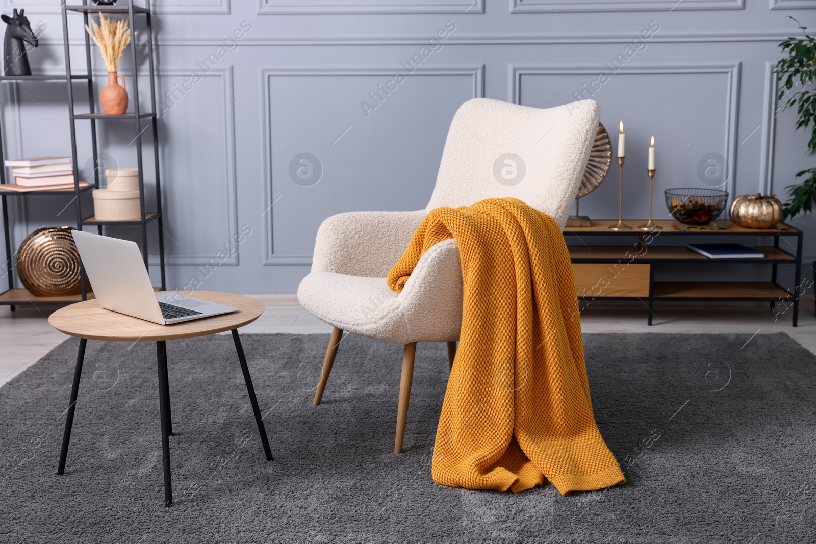 Photo of Living room interior with comfortable armchair, blanket and side table