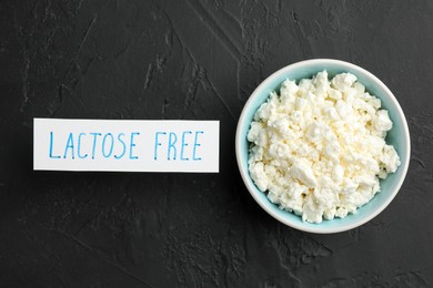 Photo of Cottage cheese and card with phrase Lactose free on black textured table, top view