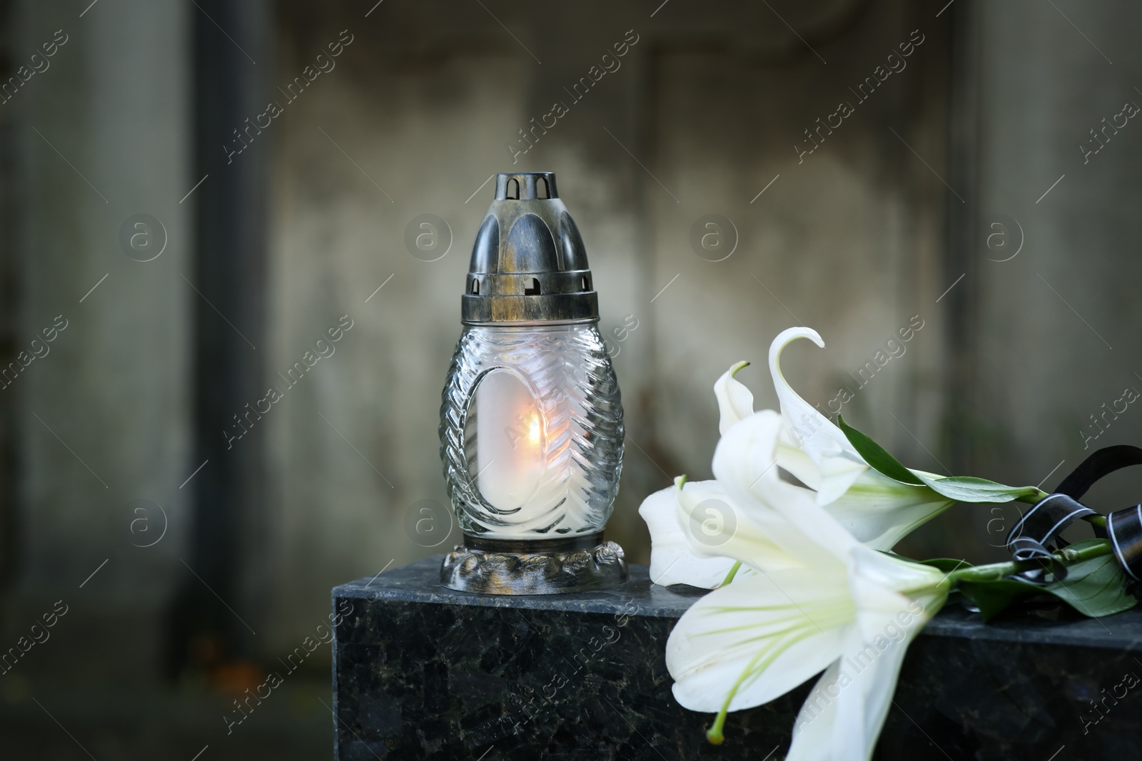 Photo of Lilies and grave lantern with burning candle on tombstone in cemetery, space for text