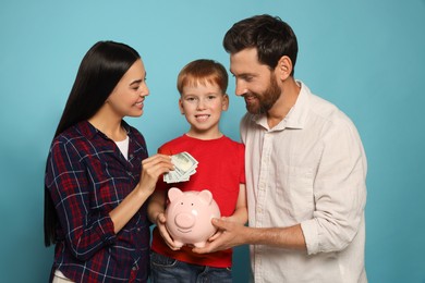 Photo of Happy family putting money into piggy bank on light blue background