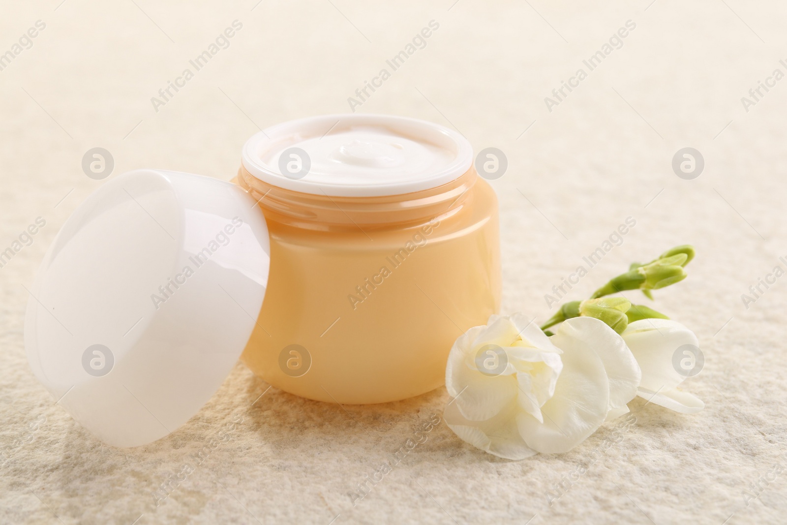 Photo of Body care. Moisturizing cream in open jar and flower on light textured table, closeup