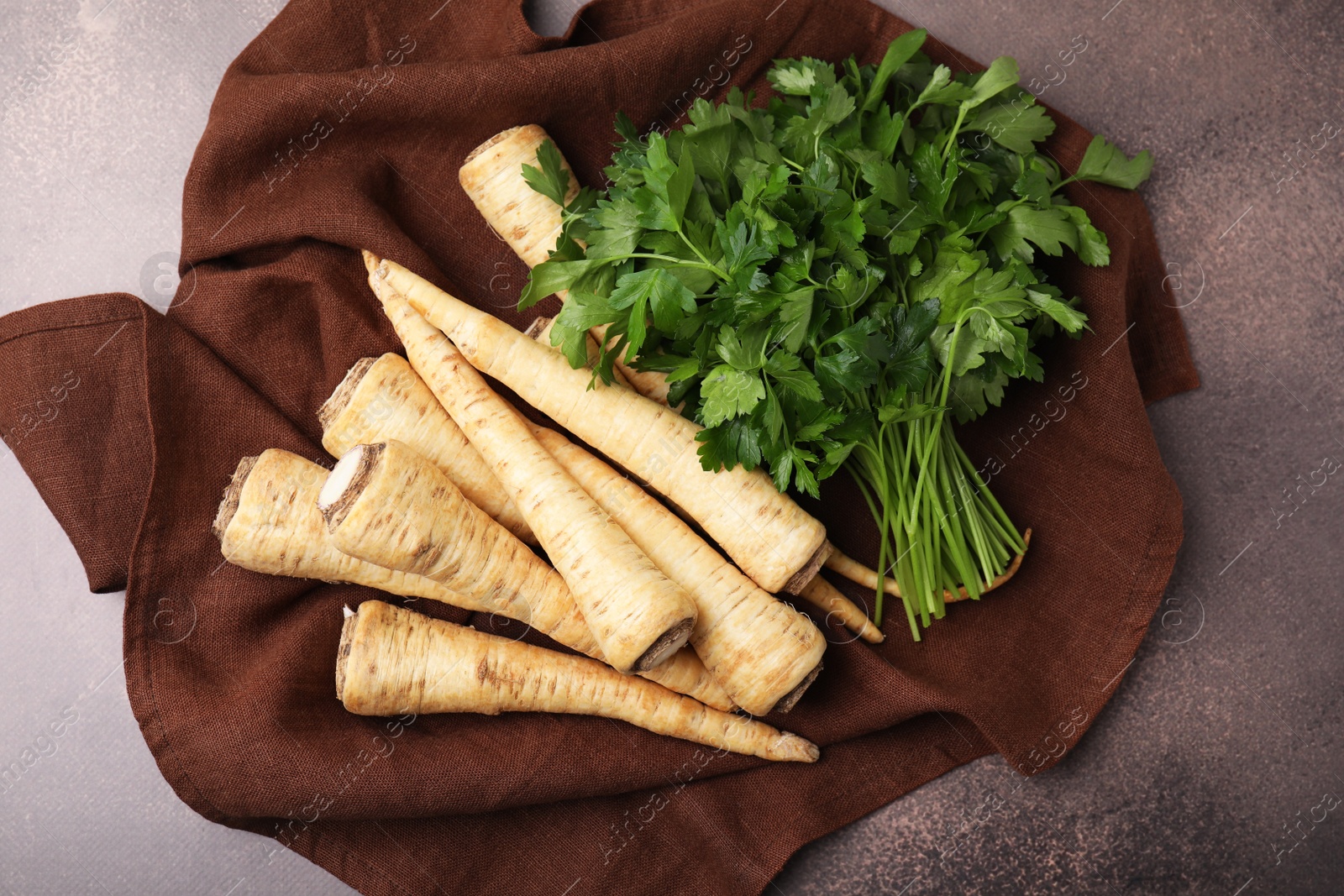 Photo of Whole raw parsley roots and bunch of fresh herb on brown table, flat lay