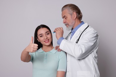 Doctor dripping medication into woman's ear on light grey background