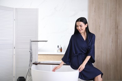 Photo of Beautiful young woman sitting on edge of tub in bathroom