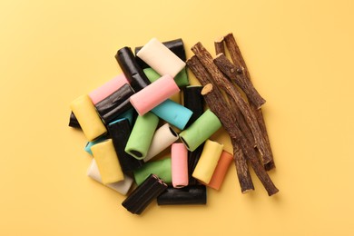 Tasty candies and dried liquorice roots on yellow background, top view