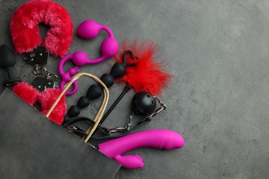 Photo of Paper shopping bag with different sex toys on grey table, flat lay. Space for text