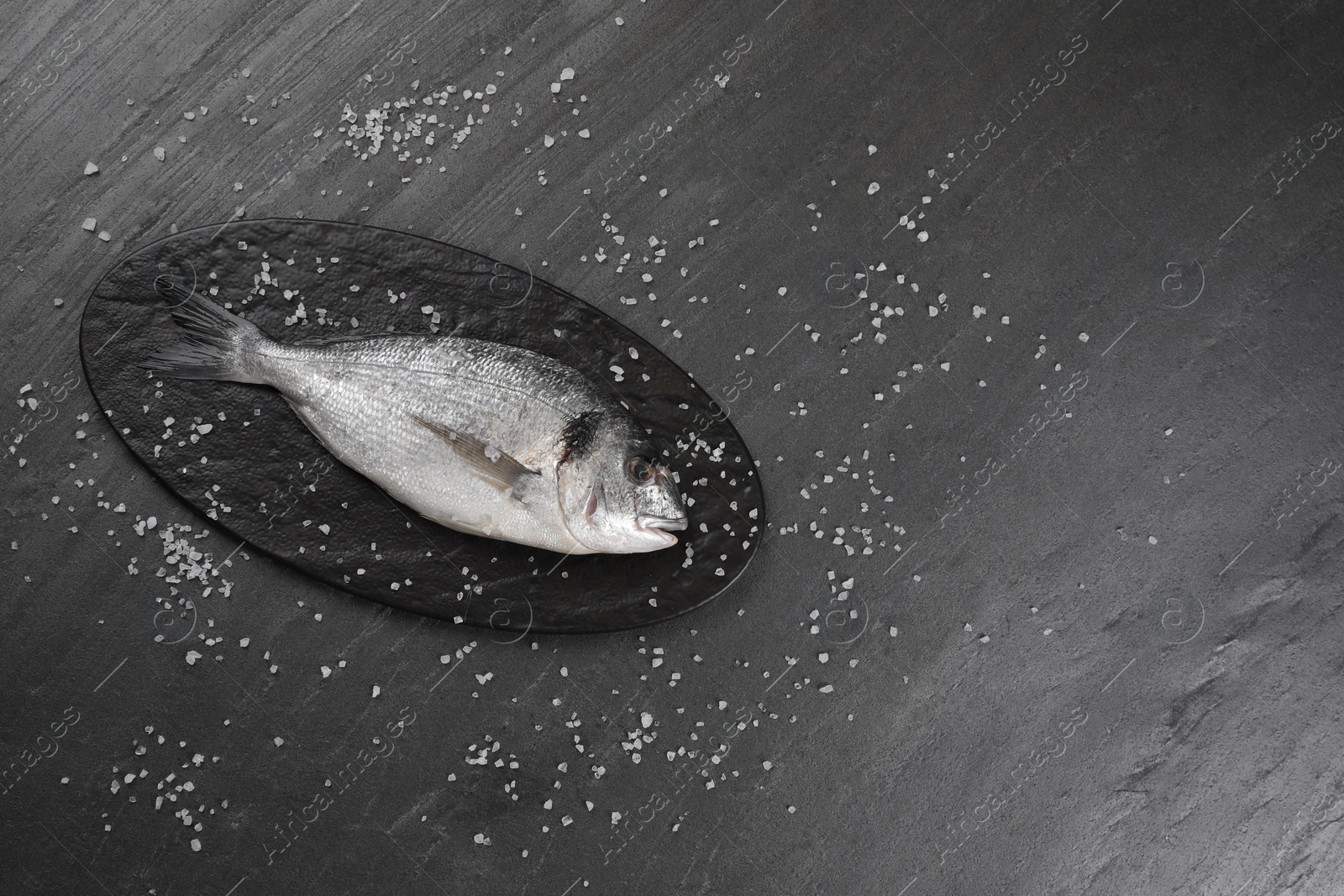Photo of Fresh raw dorado fish and sea salt on black table, flat lay. Space for text