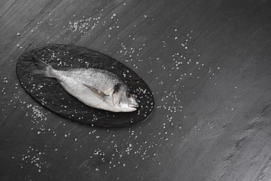 Photo of Fresh raw dorado fish and sea salt on black table, flat lay. Space for text