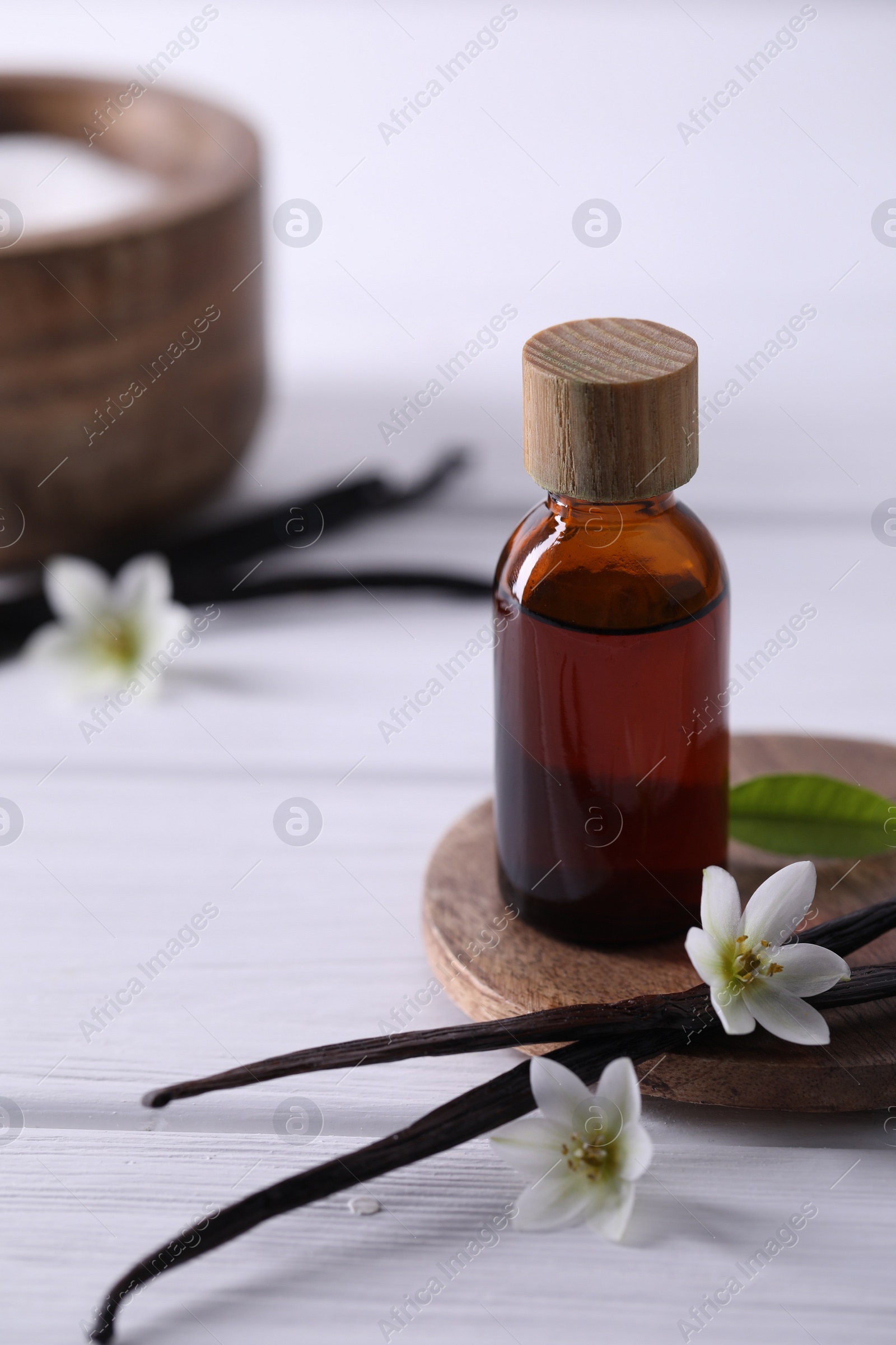 Photo of Vanilla pods, flowers and bottle with essential oil on white wooden table, closeup