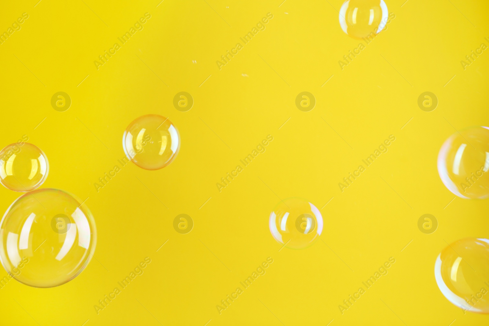 Photo of Beautiful transparent soap bubbles on yellow background