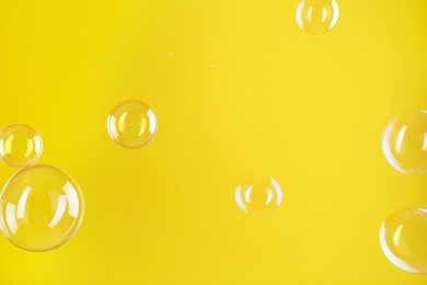 Photo of Beautiful transparent soap bubbles on yellow background