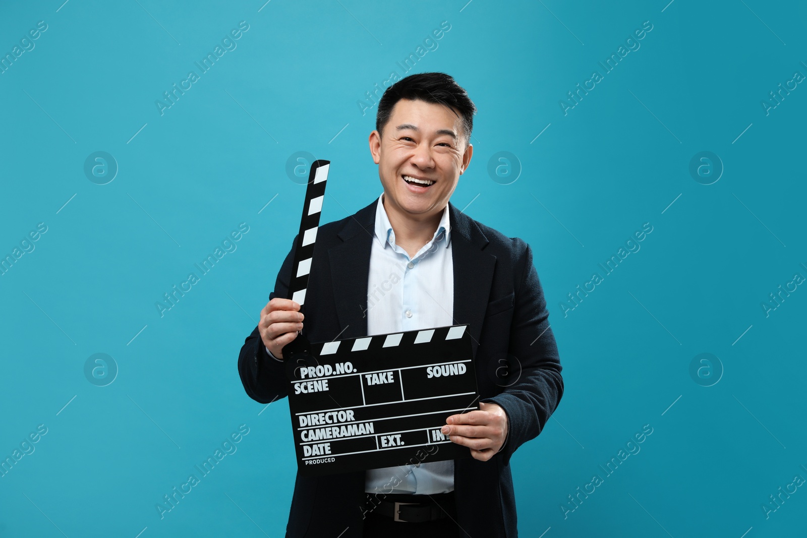 Photo of Happy asian actor with clapperboard on light blue background. Film industry