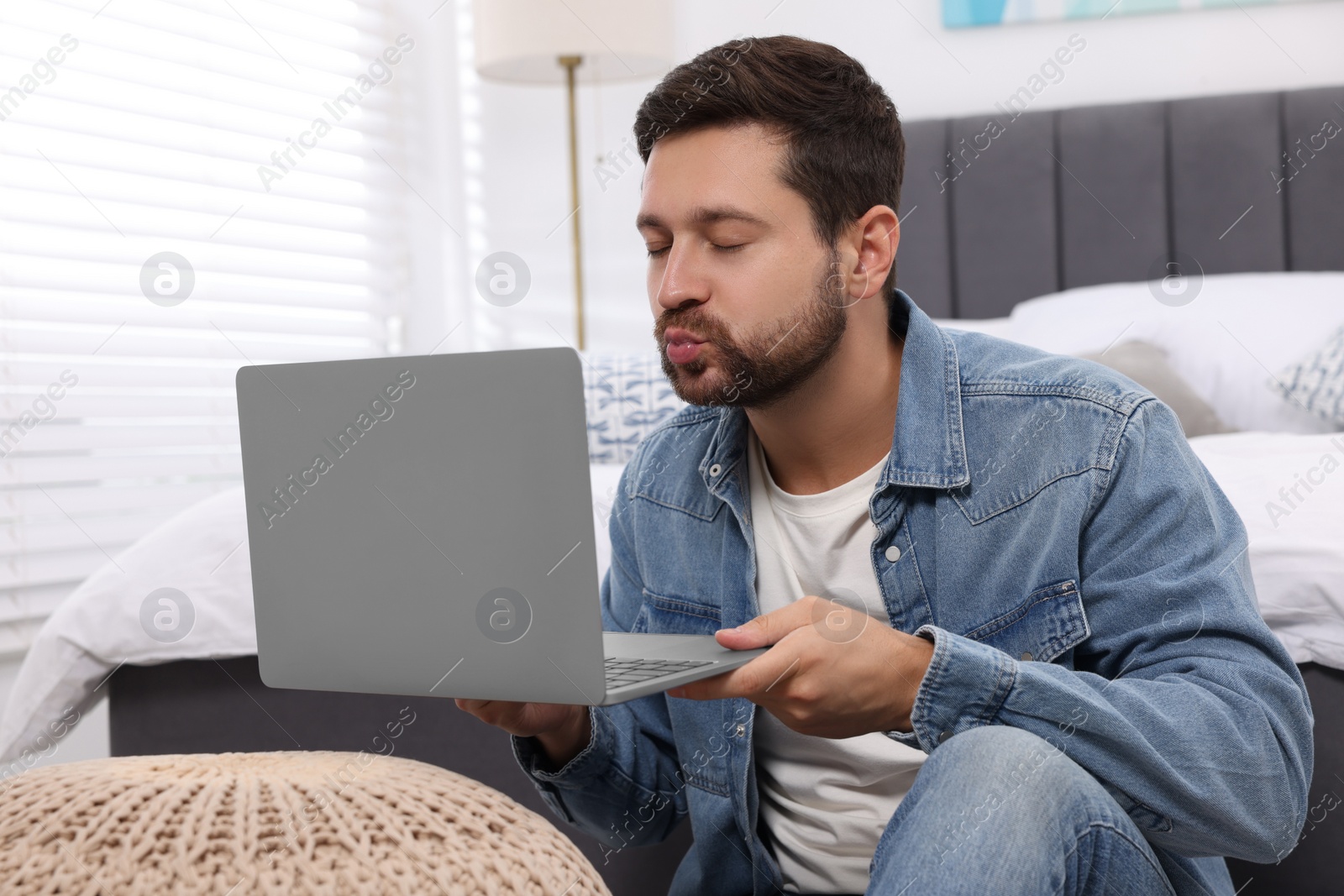 Photo of Man sending air kiss during video chat via laptop at home. Long-distance relationship