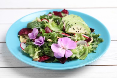 Photo of Fresh spring salad with flowers in plate on white wooden table, closeup