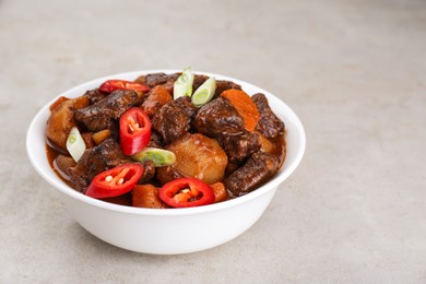 Delicious beef stew with carrots, chili peppers, green onions and potatoes on white textured table, closeup. Space for text