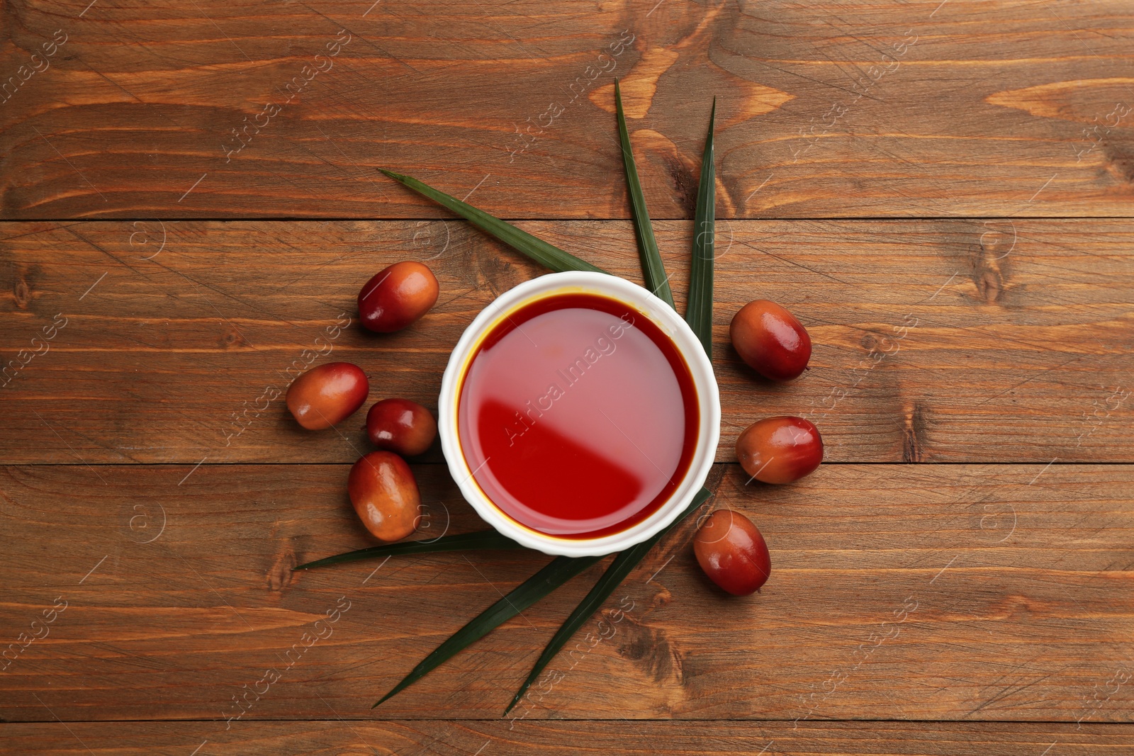 Photo of Palm oil in bowl, tropical leaf and fruits on wooden table, flat lay