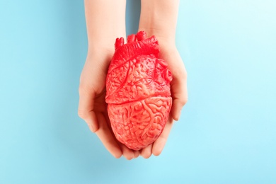 Photo of Woman holding model of heart on color background. Heart attack concept