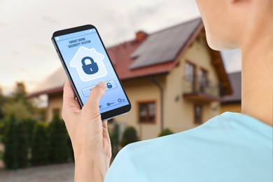 Woman using home security system application on smartphone outdoors, closeup