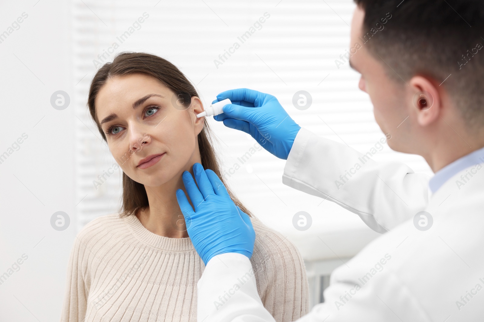 Photo of Doctor applying medical drops into woman's ear indoors