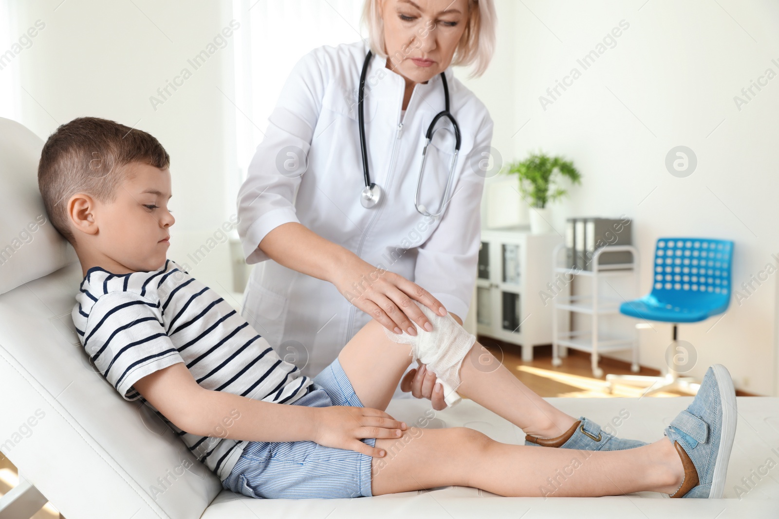 Photo of Doctor applying medical bandage to little patient's injured knee in clinic