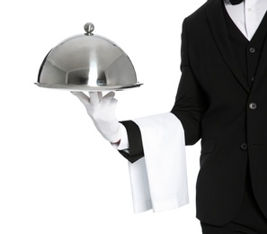 Young waiter holding metal tray with lid on white background