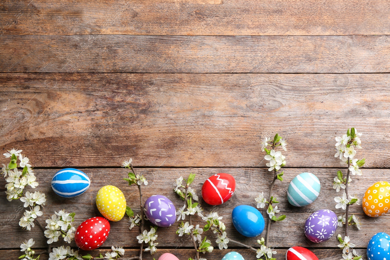 Photo of Flat lay composition with painted Easter eggs and blossoming branches on wooden background. Space for text