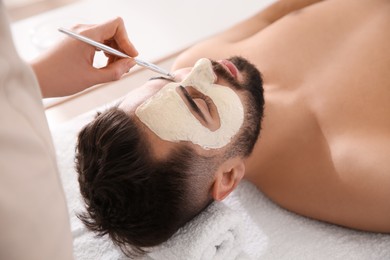 Cosmetologist applying mask on man's face in spa salon