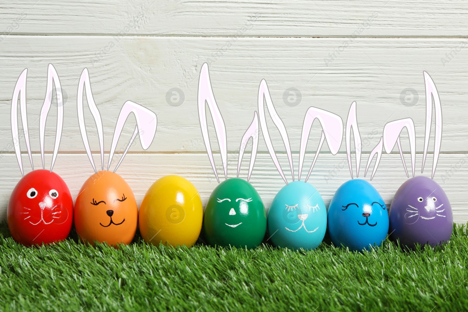 Image of Colorful eggs as Easter bunnies on green grass against wooden background