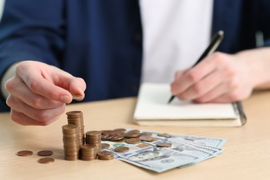 Photo of Financial savings. Man stacking coins while writing down notes at wooden table, closeup