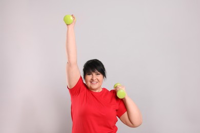 Happy overweight mature woman doing exercise with dumbbells on grey background