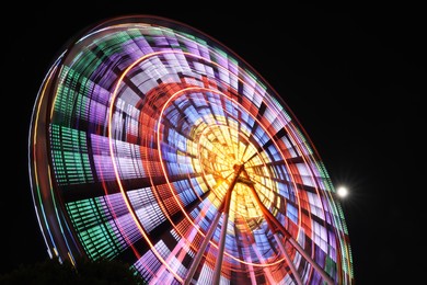 Photo of Beautiful glowing Ferris wheel against dark sky, low angle view