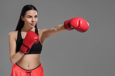 Photo of Beautiful woman in boxing gloves training on grey background. Space for text