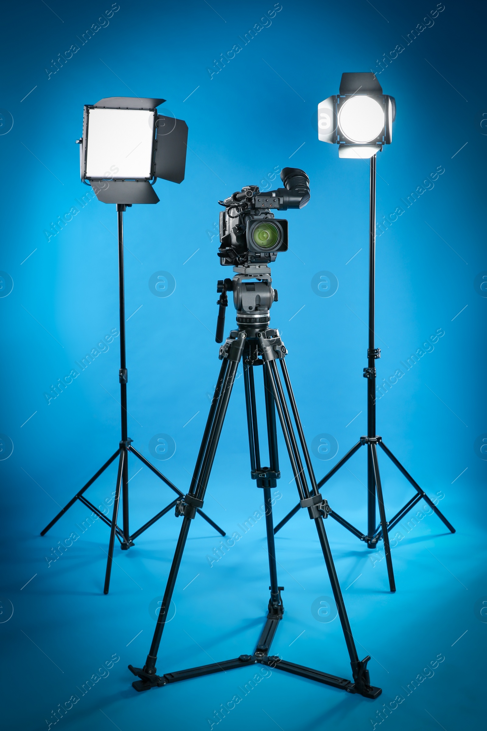 Photo of Professional video camera and lighting equipment on blue background