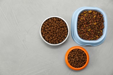 Photo of Dry food in pet bowls on grey background, flat lay. Space for text